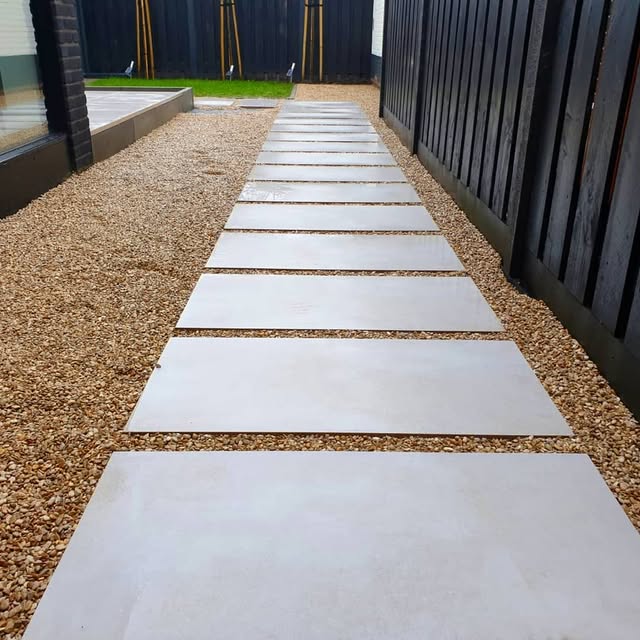 Modern tuinpad met grote tegels, grind en houten afscheiding